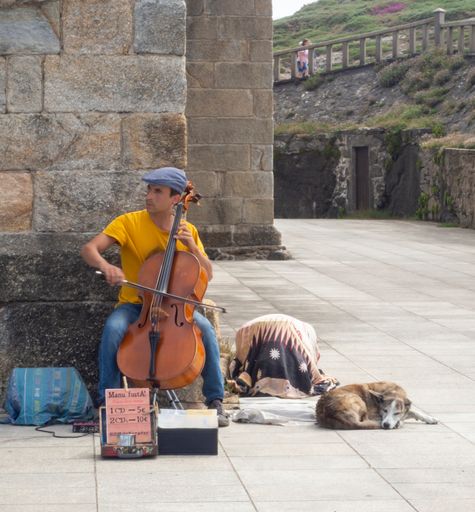 The picture shows a street musician playing the cello outside of a church.