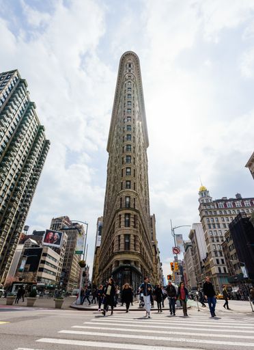 A vertical shot of people crossing the street near the flatiron building under a cloudy sky