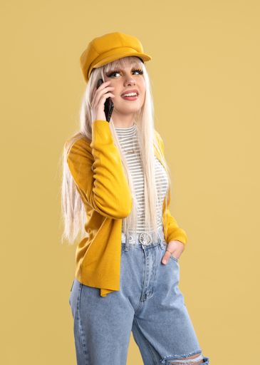 A woman in cap and yellow jacket talking on the phone on a yellow background