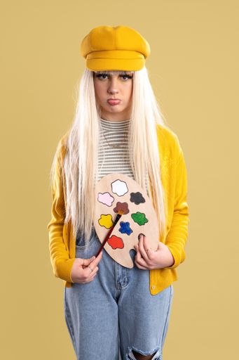 A Blonde Spanish woman with cap and paint palette on a yellow background with a sad face