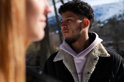 A closeup of a profile view of an unfocused woman's face in the foreground and a smiling beard man's face in profile in the background
