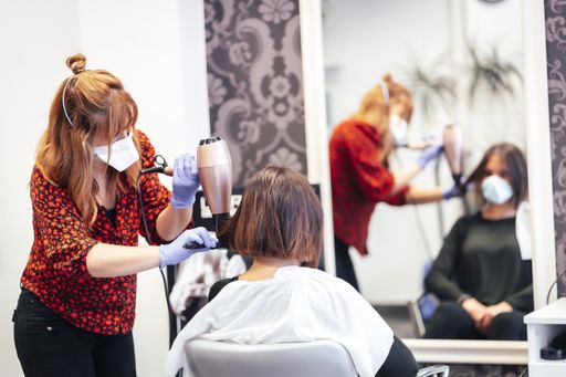 A selective focus shot of a hairdresser with mask and gloves cutting the hair of a Caucasian female