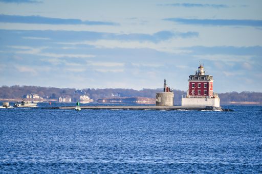 A Sub leaving the Thames River passing by New London Ledge Light escorted by a heavily armed navy boat