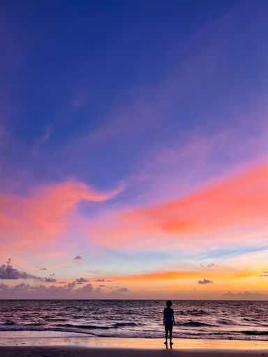 A vertical shot of the magnificent sunset and the female standing on the beach in Pernambuco, Brazil