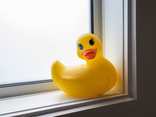 A closeup of a yellow plastic duck toy with a red beak on a window sill of a bathroom
