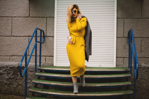 An attractive female model wearing a beautiful yellow dress and sunglasses posing near a staircase