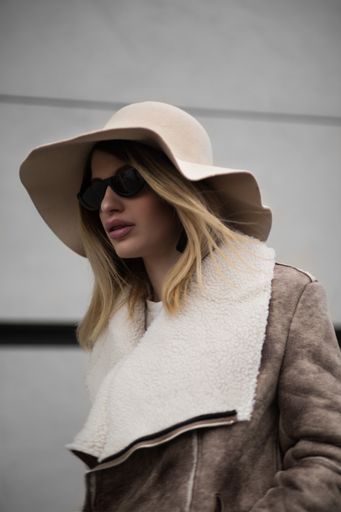 A vertical shot of an attractive female wearing a warm coat and sunglasses with a hat