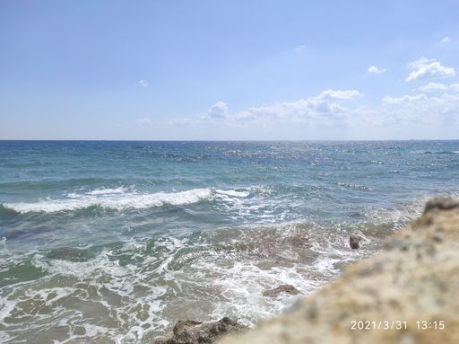 A scenic view of the ocean waves splashing against the stones on the beach under a blue sky