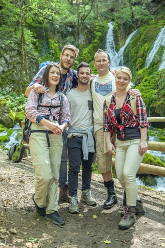 A group of friends standing in front of a beautiful waterfall on a sunny day