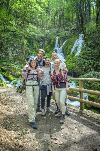 A group of happy friends posing in nature in front of a waterfall