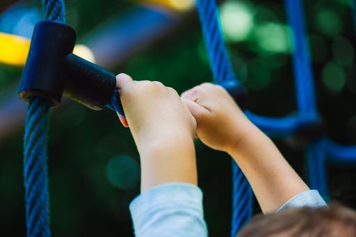 A low angle shot of a child holding on to a blue climbing toy on the playground of a park