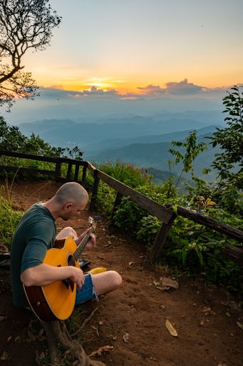 A vertical shot of a man playing guitar on mountin at sunset. Chiang Mai, Thailand