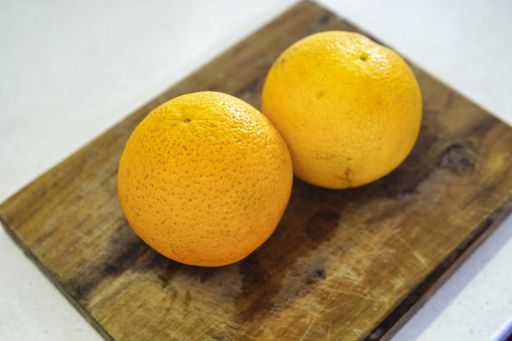 A closeup shot of two whole oranged on a wooden board isolated on a white background