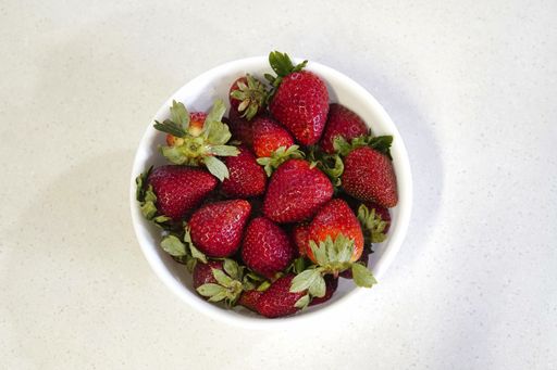 A high angle shot of fresh and delicious strawberries in a bowl isolated on a white background