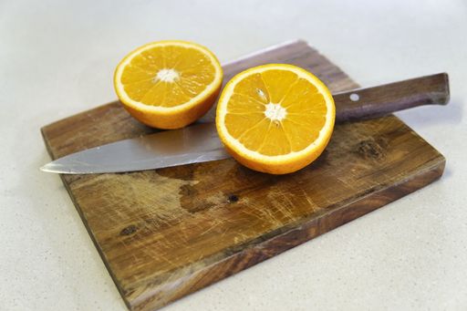 A shot of a delicious juicy orange cut in half on a wooden cutting board with a knife