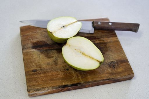 A shot of a delicious green pear cut in half on a wooden cutting board with a knife