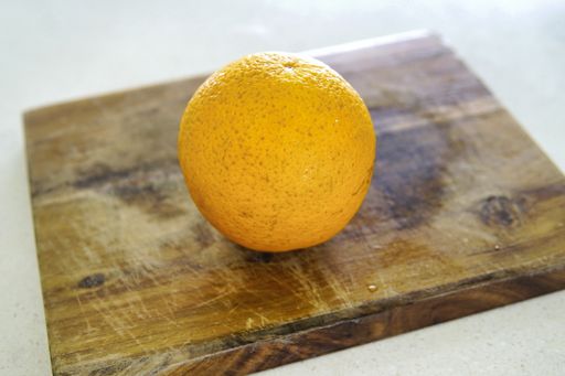 A closeup shot of a whole orange on a wooden cutting board