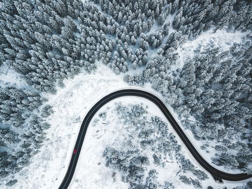 Aerial photo of a curvy road going trough the snowy forest.