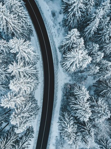 Aerial photo of a curvy road going trough the snowy forest.