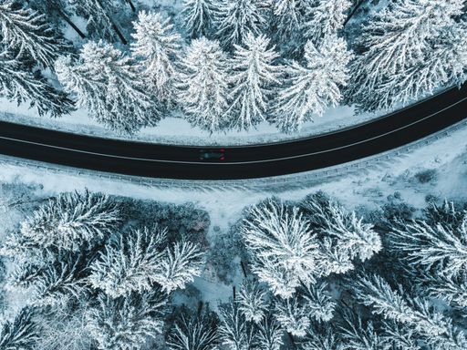 Aerial photo of a curvy road going trough the snowy forest.