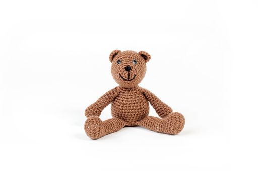 A cute brown teddy bear sitting on a white surface with a white background