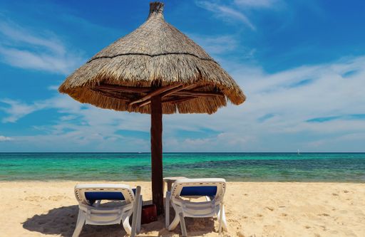 A view of a sea with two sun loungers and a wooden umbrella on the beach. Vacation concept