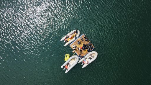 An aerial shot of the boats and the people resting on the wooden board on the lake