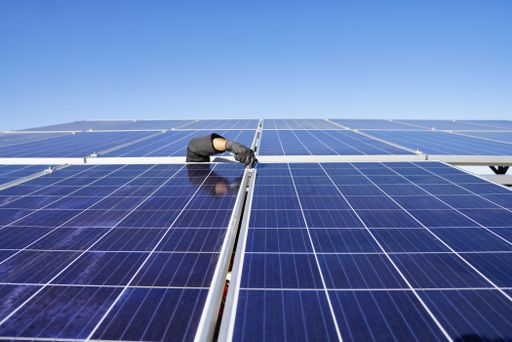 A person working on the solar panels on a roof under the sunlight at daytime - environmental concept
