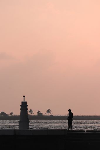 A vertical distant view of silhouette of a male and lighthouse at the coast during sunset in Maldives