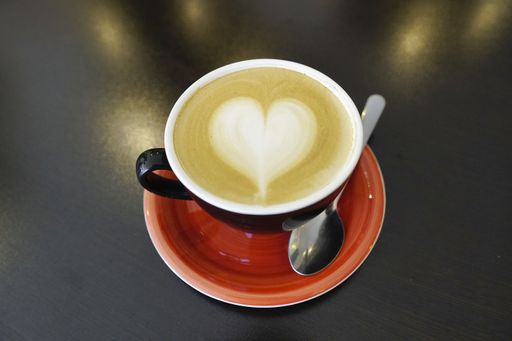 A high angle shot of a cup of latte with a heart on it on the table under the lights - perfect for drink concepts