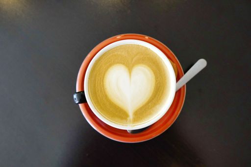 A high angle shot of a cup of latte with a heart on it on the table under the lights - perfect for drink concepts