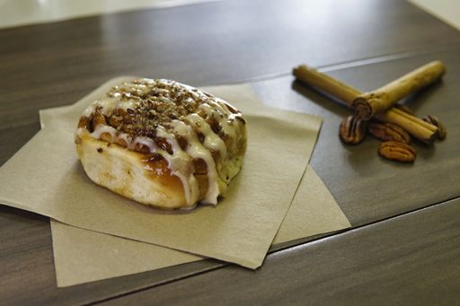 A closeup shot of a cinnamon roll on parchment papers on the table with nuts and cinnamon sticks