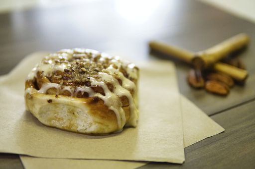 A closeup shot of a cinnamon roll on parchment papers on the table with nuts and cinnamon sticks