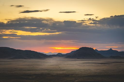 An evening view from a field with hills and dark clouds on the background