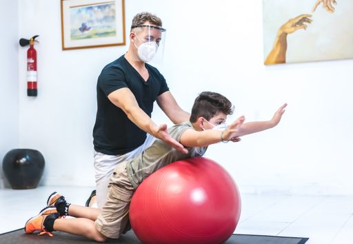 A physiotherapist wearing a face mask helping a young patient with some equipment