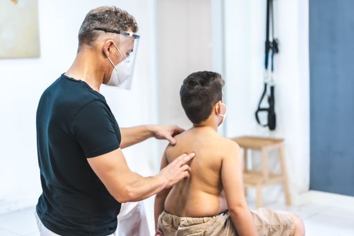 A physiotherapist wearing a face mask giving back massage to a young patient