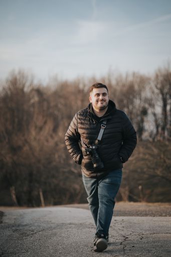 A vertical shot of a Caucasian man walking with a camera hanging on the shoulder