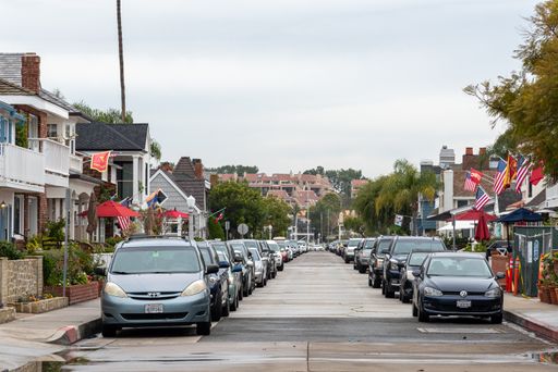 The one way street on Balboa Island with parked cars and houses with American flags.