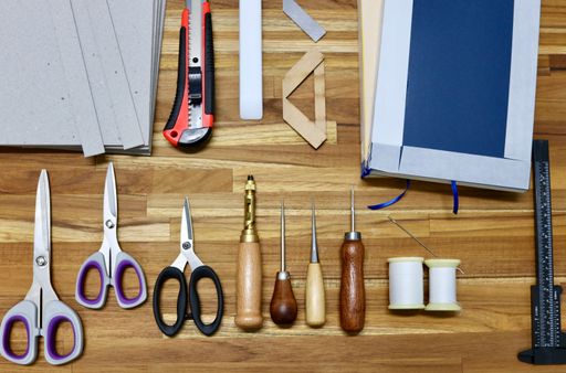 A flat lay of tools used in bookbinding process on a wooden table