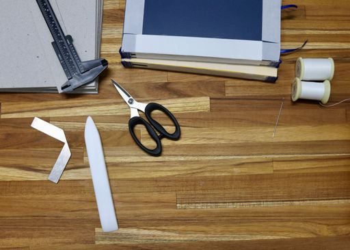 A flat lay of tools used in bookbinding process on a wooden table