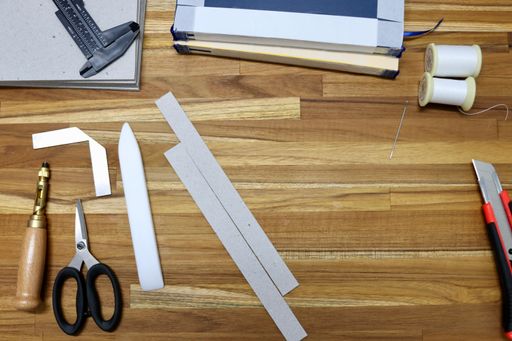 A flat lay of tools used in bookbinding process on a wooden table