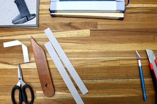 A flat lay of tools used in bookbinding process on a wooden table