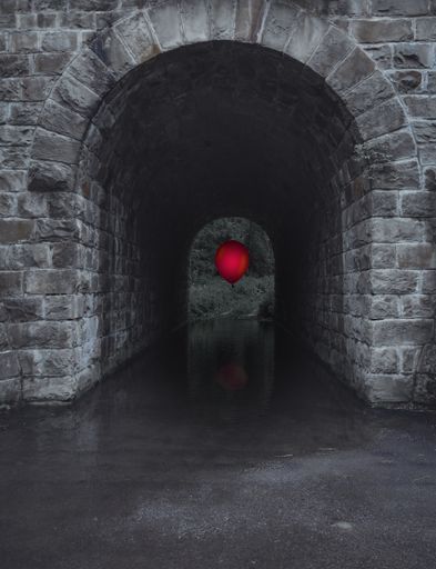 A vertical shot of a red balloon in a gray stone water tunnel