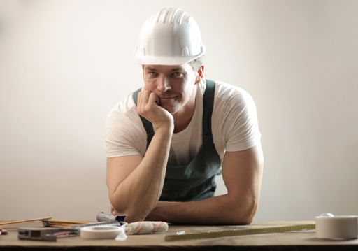 A middle-aged carpenter wearing a white hard hat and uniform against a white wall