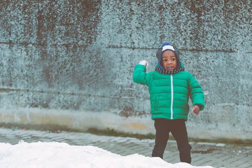 An African American kid in a green jacket playing in the yard