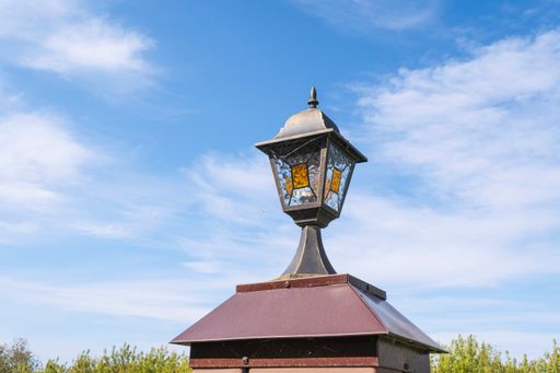 An old street lamp with broken glass against a blue cloudy summer sky.