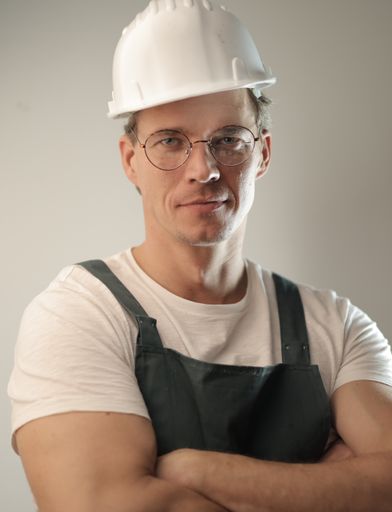 A middle-aged carpenter wearing a white hard hat and uniform against a white wall