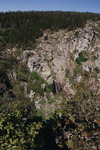 A vertical high angle shot of a small waterfall in the middle of the mountains and trees