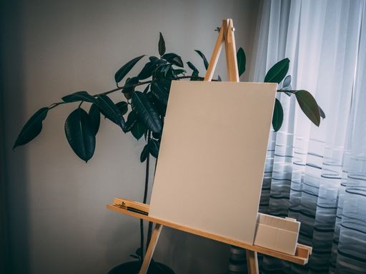 A white painting board on a wooden easel near a green plant