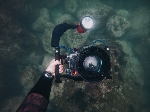 A high angle shot of a person holding a waterproof camera under the water at the bottom of the sea